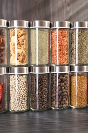 Photo of Different spices in glass jars on grey wooden table, closeup