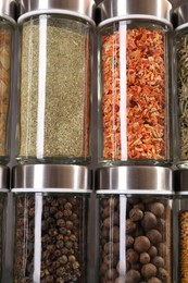Photo of Different spices in glass jars against grey background, closeup