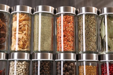 Photo of Different spices in glass jars against grey background, closeup