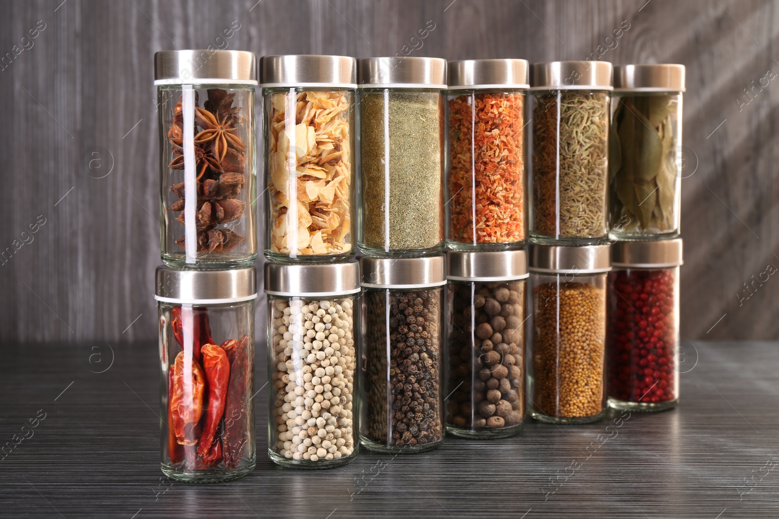 Photo of Different spices in glass jars on grey wooden table