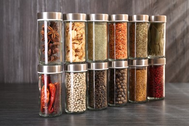 Photo of Different spices in glass jars on grey wooden table