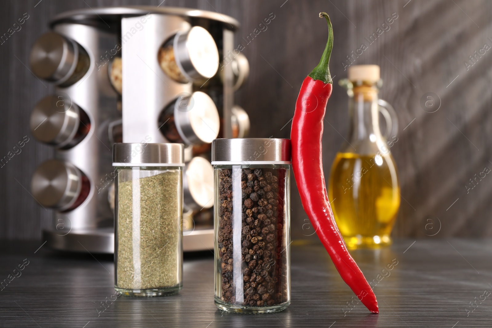 Different spices in glass jars and chili pepper on grey wooden table, closeup Photo of Different spices in glass jars and chili pepper on grey wooden table, closeup
