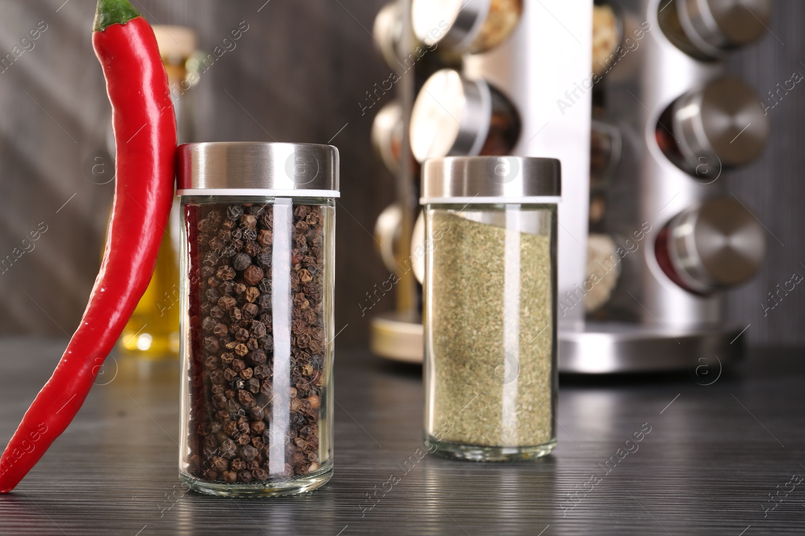 Different spices in glass jars and chili pepper on grey wooden table, closeup Photo of Different spices in glass jars and chili pepper on grey wooden table, closeup