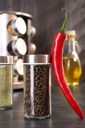 Photo of Different spices in glass jars and chili pepper on grey wooden table, closeup
