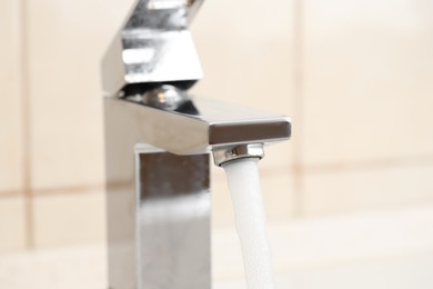 Photo of Water saving concept. Stream of water flowing from tap indoors, closeup