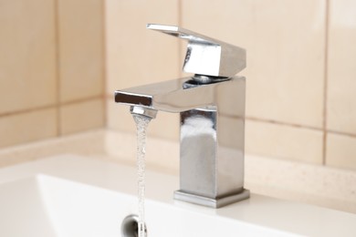 Photo of Water saving concept. Stream of water flowing from tap indoors, closeup