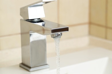Photo of Water saving concept. Stream of water flowing from tap indoors, closeup