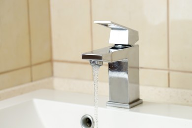 Photo of Water saving concept. Stream of water flowing from tap indoors, closeup. Space for text