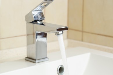 Photo of Water saving concept. Stream of water flowing from tap indoors, closeup