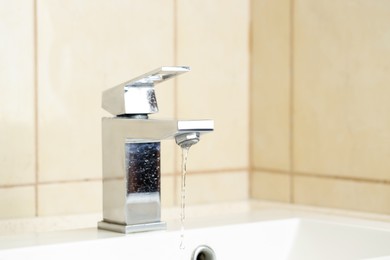 Photo of Water saving concept. Stream of water flowing from tap indoors, closeup. Space for text