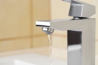 Photo of Water saving concept. Stream of water flowing from tap indoors, closeup. Space for text