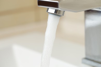 Photo of Water saving concept. Stream of water flowing from tap indoors, closeup
