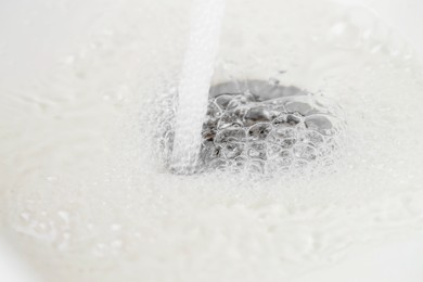 Photo of Water saving concept. Water going into sink drain, closeup