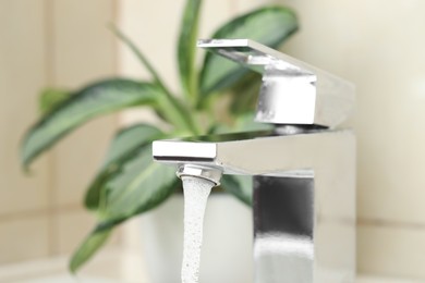 Photo of Water saving concept. Stream of water flowing from tap and houseplant indoors, selective focus