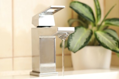 Photo of Water saving concept. Stream of water flowing from tap and houseplant indoors, selective focus