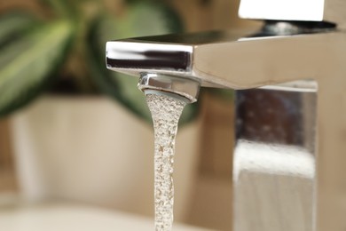 Photo of Water saving concept. Stream of water flowing from tap and houseplant indoors, selective focus