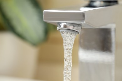 Photo of Water saving concept. Stream of water flowing from tap and houseplant indoors, selective focus. Space for text