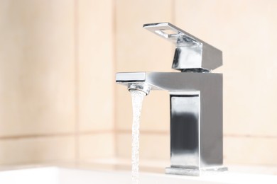 Photo of Water saving concept. Stream of water flowing from tap indoors, closeup. Space for text