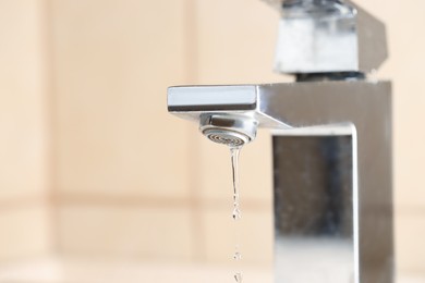 Photo of Water saving concept. Water dripping from tap indoors, closeup. Space for text