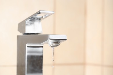 Photo of Water saving concept. Water dripping from tap indoors, closeup. Space for text