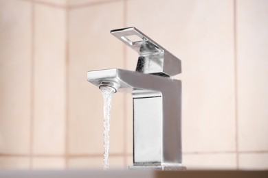 Photo of Water saving concept. Stream of water flowing from tap indoors, closeup