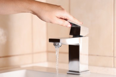 Photo of Water saving concept. Woman turning tap on indoors, closeup