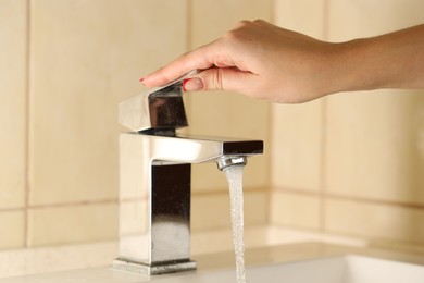 Photo of Water saving concept. Woman turning tap on indoors, closeup