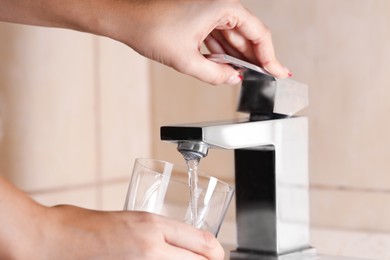 Photo of Water saving concept. Woman filling glass with tap water indoors, closeup