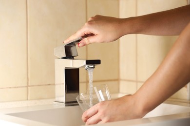 Photo of Water saving concept. Woman filling glass with tap water indoors, closeup