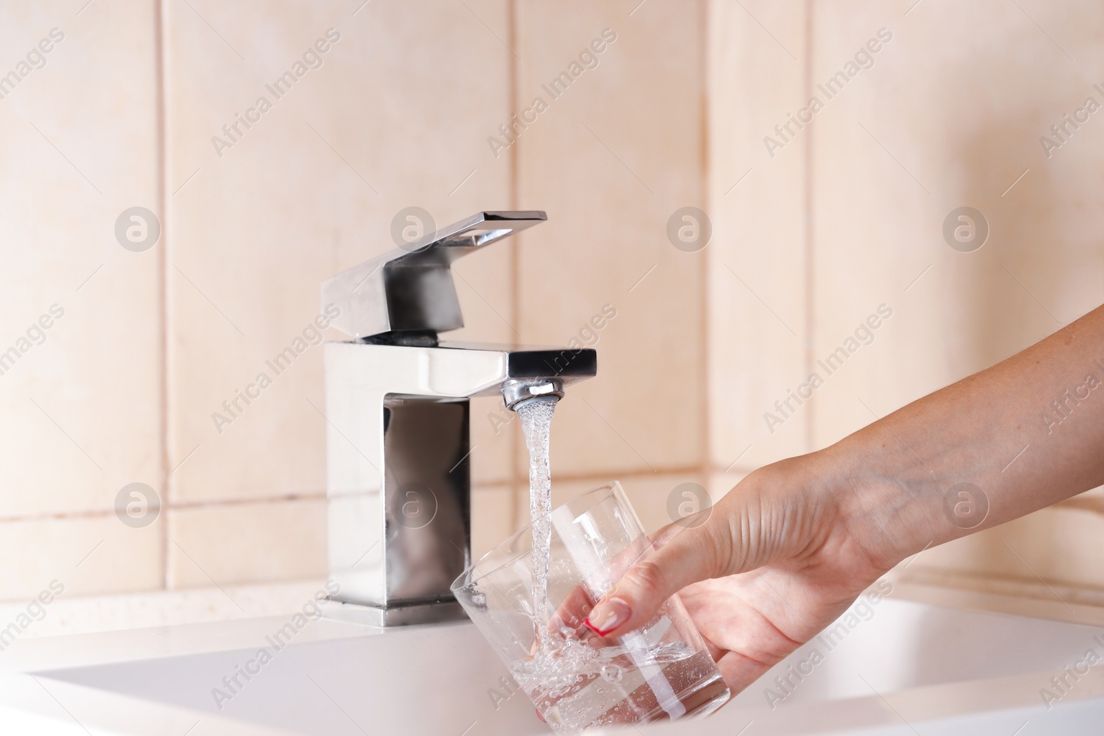 Photo of Water saving concept. Woman filling glass with tap water indoors, closeup