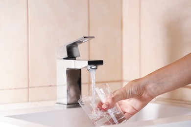 Photo of Water saving concept. Woman filling glass with tap water indoors, closeup
