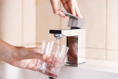 Photo of Water saving concept. Woman filling glass with tap water indoors, closeup