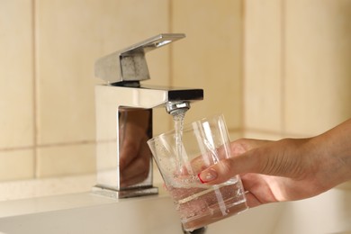 Photo of Water saving concept. Woman filling glass with tap water indoors, closeup