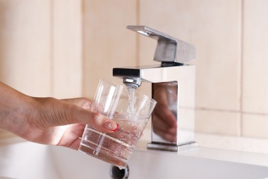Photo of Water saving concept. Woman filling glass with tap water indoors, closeup