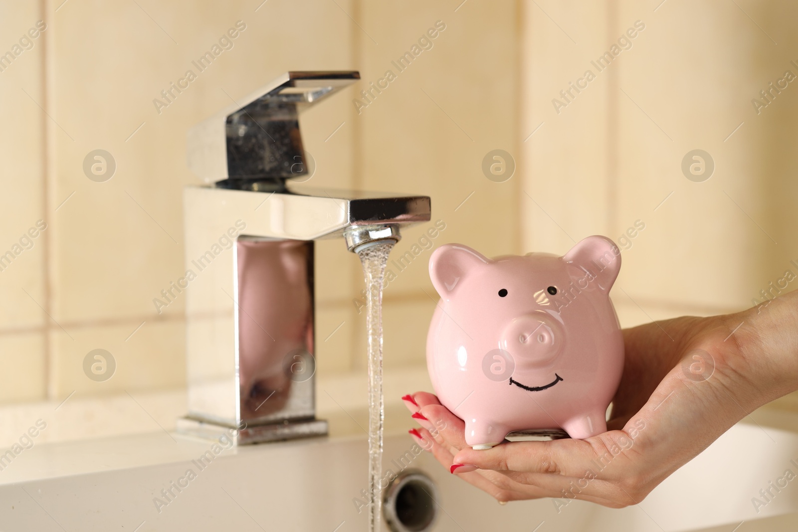 Photo of Water saving concept. Woman with piggy bank and water flowing out of tap indoors, closeup