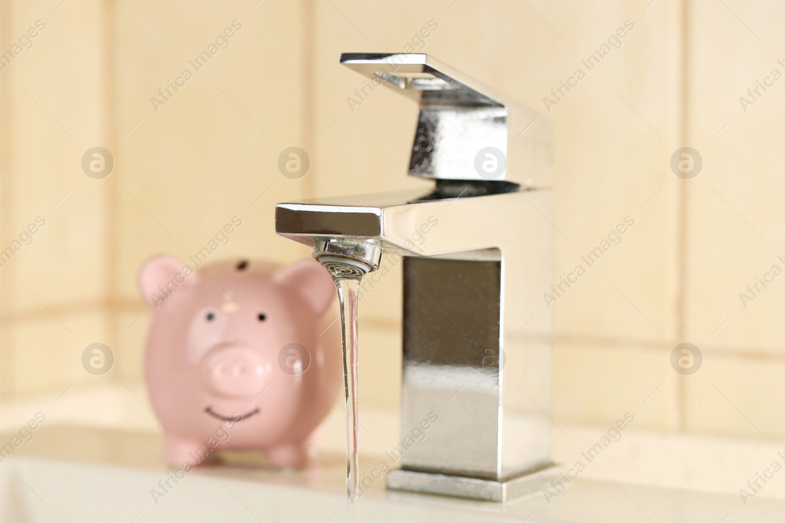 Photo of Water saving concept. Stream of water flowing from tap and piggy bank indoors, selective focus