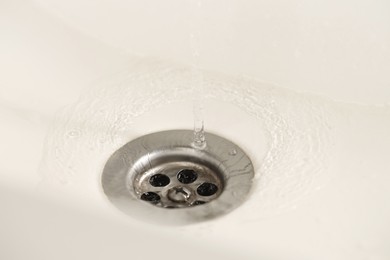 Photo of Water saving concept. Water going into sink drain, closeup