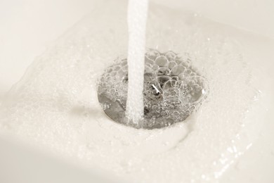 Photo of Water saving concept. Water going into sink drain, closeup