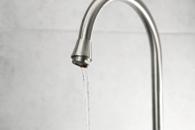 Photo of Water saving concept. Stream of water flowing from tap indoors, closeup