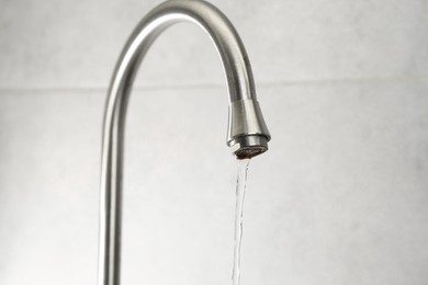 Photo of Water saving concept. Stream of water flowing from tap indoors, closeup