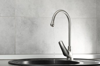 Photo of Water saving concept. Stream of water flowing from tap indoors, closeup. Space for text