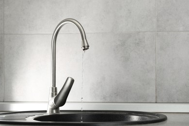 Photo of Water saving concept. Stream of water flowing from tap indoors, closeup. Space for text