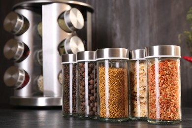 Photo of Different spices in glass jars on grey wooden table, closeup