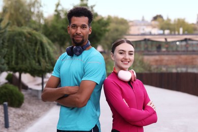Photo of Smiling runners with headphones posing with crossed arms outdoors