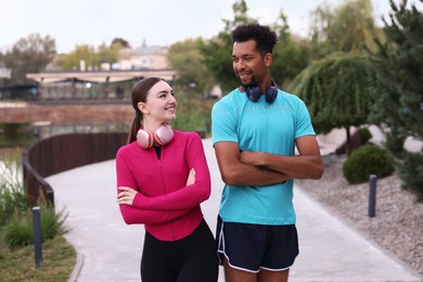 Photo of Smiling runners with headphones posing with crossed arms outdoors