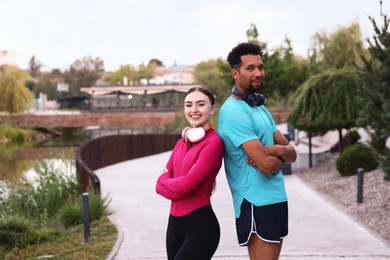 Photo of Smiling runners with headphones posing with crossed arms outdoors. Space for text