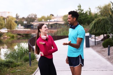 Photo of Smiling runners in sportswear with headphones talking outdoors