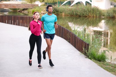 Photo of Sporty couple in headphones running near river outdoors. Space for text