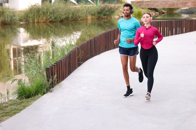 Photo of Sporty couple in headphones running near river outdoors. Space for text