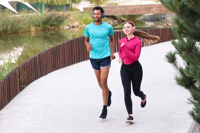Photo of Smiling couple in headphones running near river outdoors